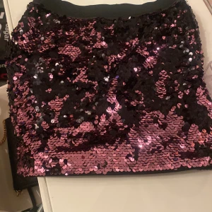 Svart och rosa paljettkjol - Snygg kortkjol täckt med glittriga paljetter i svart och rosa. Perfekt för att sticka ut på festen! Kjolen har en tight passform som framhäver figuren.