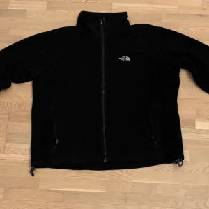 Svart fleecejacka från The North Face - Säljer en svart fleecejacka från The North Face med dragkedja framtill. Jackan har en broderad logga på bröstet och ryggen. Pris kan diskuteras !