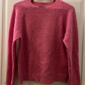 Rosa stickad tröja - Säljer en mysig rosa stickad tröja med rund hals och långa ärmar. Perfekt för kyligare dagar och ger en färgklick till din garderob. Tröjan har ribbstickade muddar vid ärmslut och nederkant. Inköpt på Vero Moda . Storlek M