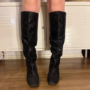 Svarta glittriga stövlar med klack - Snygga svarta boots med glitter och dragkedja på sidan. Använda 1 gång  och till annons bilderna. Dom är i nyskick förutom att klacken är lite smutsig men går lätt att ta bort. storlek 37. Nypris 800, säljes för 350.