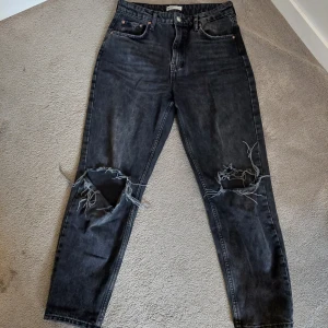Svarta jeans slitna mom jeans - Coola svarta mom jeans med slitningar på knäna. De har en klassisk femficksdesign och en bekväm passform. Perfekta för en avslappnad stil.