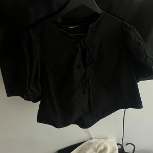 Svart blus med knytning - Snygg svart blus från Gina tricot  med knytning framtill. Blusen har korta ärmar och en lös passform, perfekt för en stilren look.