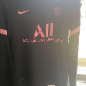 Svart PSG fotbollströja från Nike - Säljer en svart långärmad PSG fotbollströja från Nike med rosa detaljer. Tröjan har klubbens emblem och sponsorlogga i rosa på framsidan. Perfekt för fans av Paris Saint-Germain! 💖 Pris kan diskuteras vid snabb affär!!! Skriv om ni har frågor