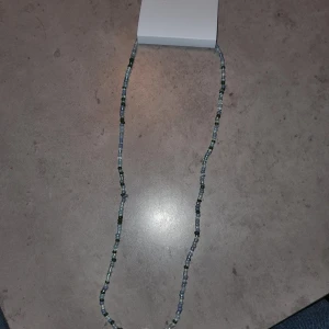 Halsband med pärlor - Snyggt halsband med små pärlor i olika färger som grönt och blått. Perfekt för att ge en färgklick till din outfit. Halsbandet är långt och kan bäras på olika sätt.