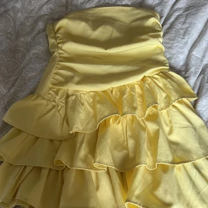 Gul axelbandslös klänning med volanger i st S - Säljer en söt gul axelbandslös klänning med flera lager volanger. Perfekt för sommarens festligheter. Klänningen har en kort längd, köpte klänningen på plick förra sommaren och står ingen lapp så vet inte vart klänningen är ifrån☺️Men den är så fin och jätte skön att ha på sommaren då den är lite luftig🌴☀️🥰