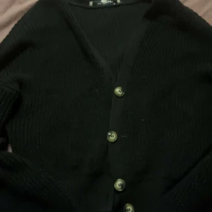 Svart kofta från KappAhl - Säljer en stilren svart kofta från KappAhl i storlek S. Koftan har en v-ringad design med knappar framtill och är perfekt för alla årstider. Den är mjuk och bekväm att bära.