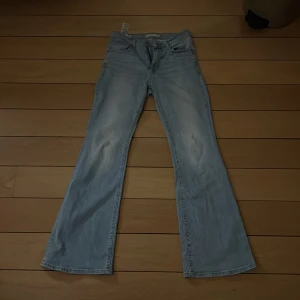 Ljusblå bootcut jeans från Levi's - Snygga ljusblå bootcut jeans från Levi's med klassisk femficksdesign och knappgylf. Perfekta för en avslappnad stil med en touch av retro. Levi's logga syns på bakfickan.