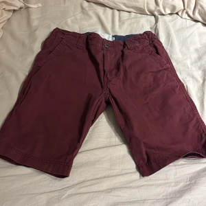 Vinröda shorts med knappstängning - Snygga vinröda shorts med knappstängning och dragkedja. De har en klassisk passform med fickor både fram och bak. Perfekta för en avslappnad stil under varmare dagar.