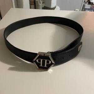 Svart bälte från Philipp Plein - Snyggt svart bälte från Philipp Plein med en stilren silverfärgad spänne i form av en hexagon. Tillverkat i Italien med högkvalitativt skinn. Perfekt för att ge en lyxig touch till din outfit.