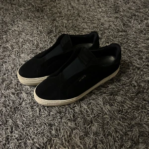 Mörkblåa sneakers från Axel Arigato - Snygga mörk blås sneakers från Axel Arigato i mocka med en stilren design. Skorna har en vit sula och är perfekta för en casual look. De är i storlek herr 43 och har en diskret logga på sidan. Box och påse ingår!