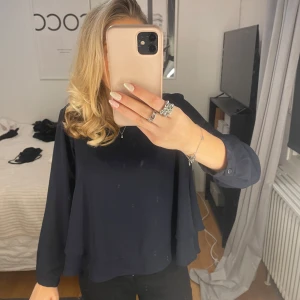 Mörkblå blus med volangdetaljer - Snygg mörkblå blus med volangdetaljer på ärmarna. Perfekt för en stilren look. Blusen har långa ärmar och en lös passform.❤️❤️