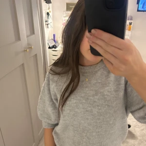 Grå stickad tröja - Mysig grå stickad tröja med rund hals och trekvartsärmar. Perfekt för kyligare dagar och enkel att matcha med olika outfits.