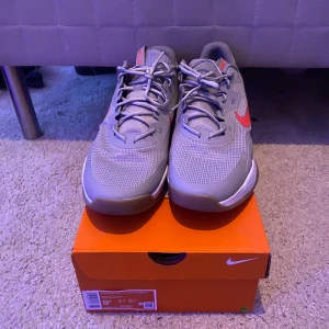 Nike gym skor  - Snygga grå Nike sneakers med röda detaljer och snörning. Skorna har en modern design med en synlig dämpning i hälen och en bekväm passform. Perfekta för både träning och vardag. Pris kan diskuteras vid snabb affär!