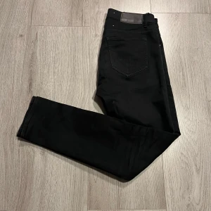 Svarta jeans från Tiger of Sweden - Snygga svarta jeans från Tiger of Sweden med en klassisk design. De har en rak passform och är tillverkade i ett slitstarkt material. Perfekta för en stilren look.