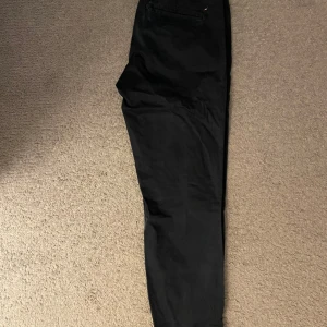 Mörkblåa chinos från Boomerang - Snygga Mörkblåa chinos från Boomerang med en broderad detalj. Byxorna har en klassisk passform och är tillverkade i bomull för en bekväm känsla. Storlek 31 32. Hör gärna av er vid funderingar:)