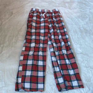 Rutiga pyjamasbyxor från Lindex - Säljer ett par bekväma och stiliga rutiga byxor från Lindex. Byxorna har ett klassiskt rödvitt rutmönster och är utrustade med en praktisk snörning i midjan. Perfekta för en avslappnad look.