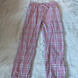 Rosa rutiga byxor från Lindex - Säljer ett par bekväma rosa byxor från Lindex med rutigt mönster. Byxorna har en elastisk midja med snörning för extra komfort. Perfekta för en avslappnad stil.