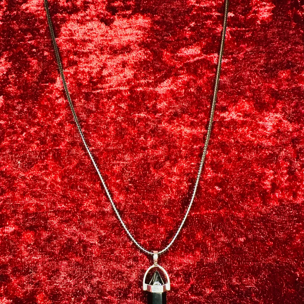 Elegant halsband med en svart kristallhänge infattad i silver. Kedjan är tunn och smidig, vilket ger en stilren look. Perfekt för att lägga till en touch av mystik till din outfit.. Asusteet.