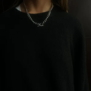 011 - Stilrent silverfärgat halsband med en kedjedesign. Perfekt för att ge en elegant touch till din outfit. Halsbandet har en enkel och modern look.