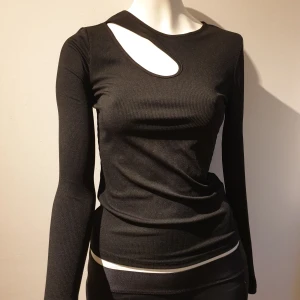 Svart ribbad topp  - Snygg svart ribbad topp från SHEIN med unik cut-out detalj vid halsen. Den har långa ärmar och en tight passform som framhäver figuren. Perfekt för en trendig look.