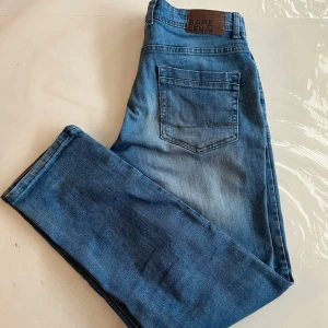 Blå jeans från Bare Denim - Snygga blå jeans från Bare Denim i modellen slim straight. De har en klassisk femficksdesign och en knappgylf. Perfekta för en stilren look.