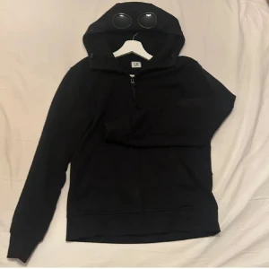 Cp company hoodie  - Säljer en svart hoodie från C.P. Company med unika glasögon på huvan. Perfekt för en cool och avslappnad stil. Passar bra till både vardag och speciella tillfällen. Kom privat för minsta frågor eller funderingar, kan skicka fler bilder och sänka priset vid snabb affär
