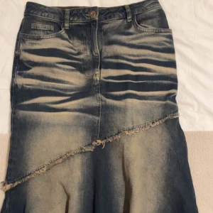 Jeanskjol med fransdetalj - Snygg jeanskjol med unik fransdetalj och asymmetrisk design. Kjolen har en klassisk jeansfärg och är perfekt för en avslappnad stil. Den har fickor både fram och bak samt en rå kant som ger en cool touch. Köpta från beyond retro skriv vid intresse för bättre bilder! 