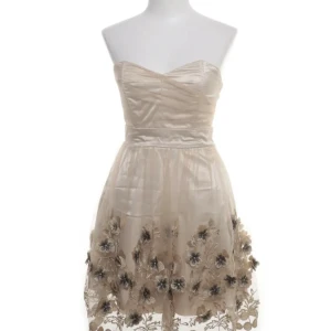 Superfin festklänning i guld med blomdetaljer - Superfin festklänning i storlek 34/36. Den är guld och har små blommor nertill. Passar perfekt till fester! Skriv gärna om ni har frågor 🤗🌸. 