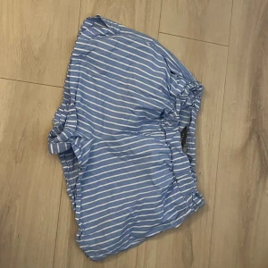 Blå- och vitrandiga shorts - Säljer ett par blå- och vitrandiga shorts med knytning i midjan. Perfekta för en avslappnad sommarlook. De har en loose passform och är tillverkade i ett lätt och bekvämt material.