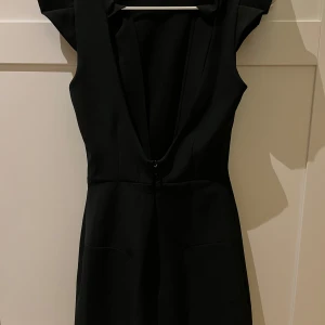 Svart klänning med knytband - Elegant svart klänning med djup v-ringning och knytband i ryggen. Perfekt för en kväll ute eller en speciell tillställning.