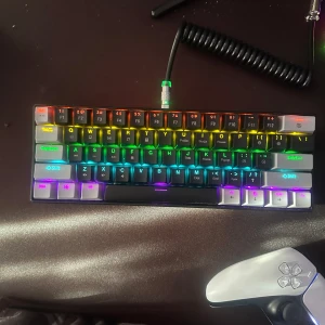 RGB Mekaniskt Tangentbord - Säljer ett RGB mekaniskt tangentbord med avtagbara keycaps och blå switchar. Tangentbordet har en kompakt design och en spiralformad kabel. Perfekt för gaming och programmering med sina färgglada bakgrundsbelysningar.