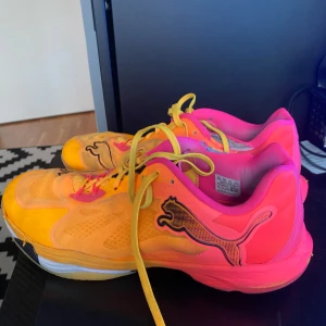 Färgglada sneakers från Puma - Säljer ett par färgglada sneakers från Puma i orange och rosa med gula snören. Skorna har en sportig design med Puma-loggan på sidan. Perfekta för dig som gillar att sticka ut!