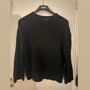 Svart stickad tröja - Säljer en klassisk svart stickad tröja med kabelstickat mönster. Tröjan har långa ärmar och en rund halsringning. Perfekt för kyligare dagar.