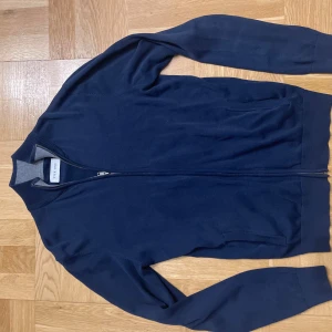 Mörkblå tröja med dragkedja från Pier One - Snygg mörkblå tröja från Pier One med dragkedja framtill. Tröjan har en ribbad krage i grått och långa ärmar. Perfekt för en stilren och avslappnad look.