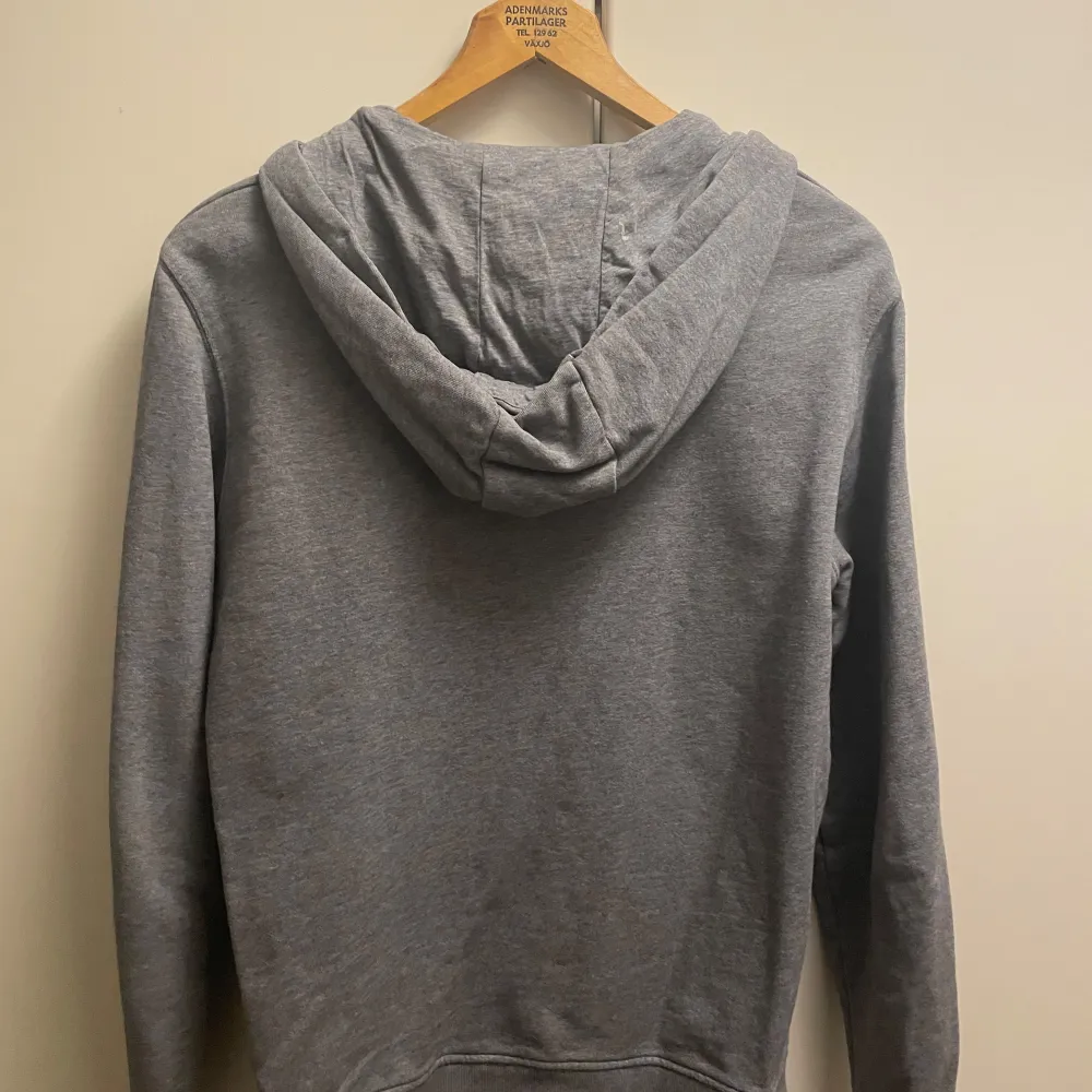 Säljer en stilren grå hoodie från Lyle & Scott med dragkedja och huva. Den har ett broderat gult emblem på bröstet och praktiska fickor framtill. Perfekt för en avslappnad look.. Neuletakit & Villapaidat.
