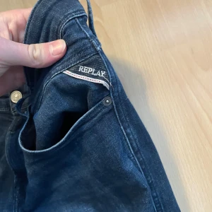 Mörkblå jeans från Replay - Snygga mörkblå jeans från Replay med klassisk femficksdesign och knappgylf. Perfekta för en stilren look. Märkesdetaljer syns vid fickan och insidan av midjan.
