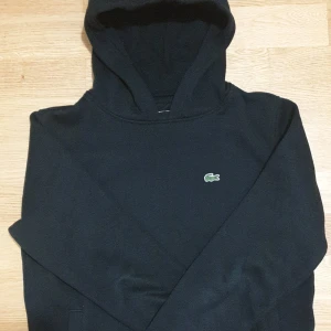 Svart hoodie från Lacoste - Nypris-1500 KR                          Säljer en stilren svart hoodie från Lacoste med den klassiska krokodilloggan på bröstet. Perfekt för en avslappnad look. Hoodien har långa ärmar och en bekväm huva.