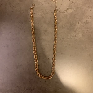 Guldigt tvinnat halsband - Elegant guldigt halsband med tvinnad design. Perfekt för att ge en touch av glamour till din outfit. Haldbandet är inte äkta guld