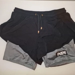 Svarta shorts från Elly Pistol - Snygga svarta shorts från Elly Pistol med grå innerbyxa. Perfekta för löprundan. Garderobsrensning så kika gärna på övriga auktioner.