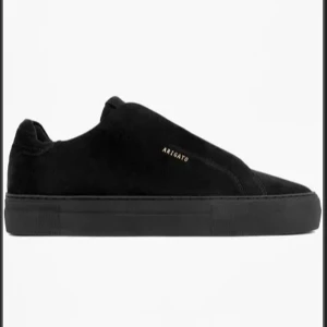 Svarta sneakers från Axel Arigato - Stilrena svarta sneakers i mocka från Axel Arigato med diskret logotyp i guld på sidan. Skorna har en minimalistisk design med en låg profil och en solid svart sula.