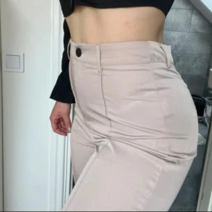 Beige kostymbyxor - Snygga beige kostymbyxor med hög midja och en stilren design. Byxorna har en knapp och dragkedja framtill, vilket ger en klassisk look. Perfekta för en chic och elegant stil.