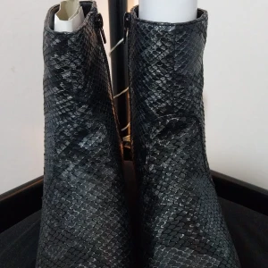 Svarta boots med ormskinnsmönster - Snygga svarta boots med ormskinnsmönster och en bekväm klack. De har en dragkedja på sidan för enkel på- och avtagning. Perfekta för att ge en edgy touch till din outfit.