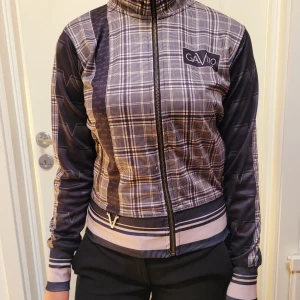 Gavelo jacka  - Snygg rutig jacka från Gavio med dragkedja framtill. Jackan har en hög krage och långa ärmar. Den är mönstrad med rutor i svart och grått och har ribbade muddar i midjan och vid ärmsluten. Perfekt för en stilren look! Gavelo! 