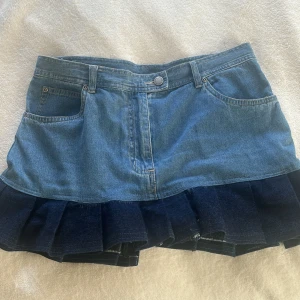 Jeanskjol med volang från Salsa - Trendig jeanskjol från Salsa med en snygg volangdetalj i mörkare denim. Kjolen har klassiska femficksdetaljer och en knappstängning fram. Perfekt för en avslappnad och stilren look.