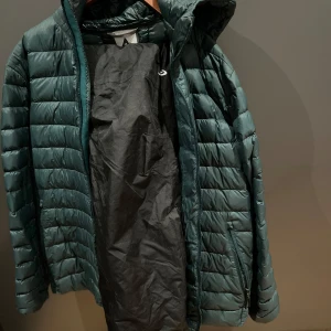 Grön dunjacka med huva och svarta täckbyxor, ett klädpaket jacka Mc Kinley five season täckbyxor - Säljer en grön dunjacka med huva. Jackan har en dragkedja framtill och är quiltad för extra värme. Perfekt för kyligare dagar. 