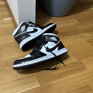 Jordan 1 panda - Snygga svartvita Nike sneakers med klassisk design. Skorna har en hög modell med snörning och den ikoniska Nike-loggan på sidan. Perfekta för en stilren look. Tror de rep1