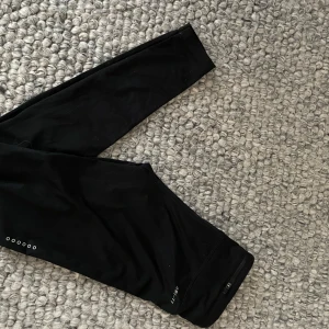 Svarta träningstights från Nike - Snygga svarta träningstights från Nike med en liten logga på benet. Perfekta för träning eller en avslappnad dag. De är tillverkade i ett stretchigt material som ger en bekväm passform.