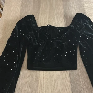 Svart sammetstopp med glittriga detaljer från Bershka - Snygg svart festlig sammetstopp från New Yorker med glittriga prickar och långa ärmar. Används 1 gång.