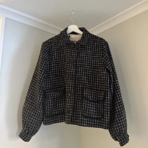 jacka från Mos Mosh - Snygg svartvit rutig jacka från Mos Mosh med stora knappar och två framfickor. Jackan har en klassisk krage och långa ärmar, perfekt för en stilren look. Den är tillverkad i ett mjukt material som ger en bekväm passform. Ena metall fliken är sönder