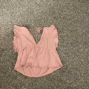 Rosa omlottopp från lager 157 - Säljer en söt rosa omlottopp från lager 157. Toppen har en v-ringning och knytband i ryggen. Den är kortärmad med volangdetaljer och har en luftig passform. Perfekt för varma dagar!